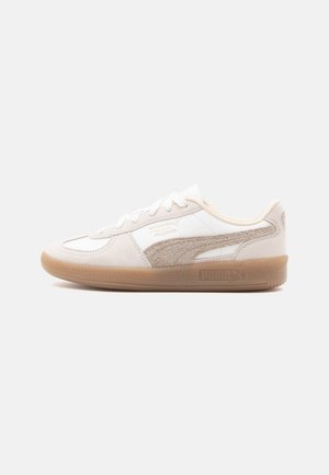 Zapatillas blancas y beige con un upper de cuero y gamuza, punta redondeada, cierre con cordones y suela de goma texturizada. Logotipo en el costado.