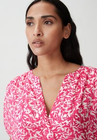 Blusa a fiori rosa con scollatura a V, maniche corte e vestibilità ampia, realizzata in tessuto leggero.