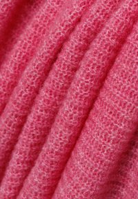 Gestructureerde roze stof met een zachte, pluizige uitstraling, die een licht gemêleerd patroon heeft en meerdere plooien in het materiaal vertoont.