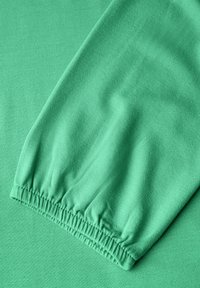 Zielony materiał o teksturowanej powierzchni. Cechuje się marszczonym mankietem na końcu rękawa. Gładki, elastyczny materiał.