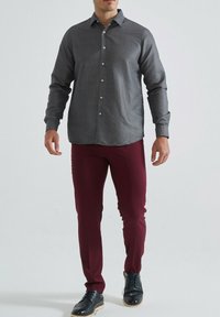 Chemise boutonnée grise à motifs avec une coupe ajustée, associée à un pantalon bourgogne slim-fit et des chaussures noires à lacets, sur un fond uni.