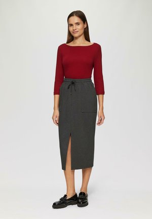 Rode lange mouwen top gecombineerd met een grijze midi rok met een voorkap en zijzakken, aangevuld met zwarte instappers.