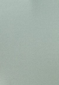 Tela de color verde claro con relieve y textura suave, con líneas verticales y un estiramiento constante, adecuada para diversas prendas.