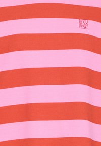 Růžová a červená látka s horizontálními pruhy a malým čtvercovým vyšívaným logem poblíž horní pravé části.