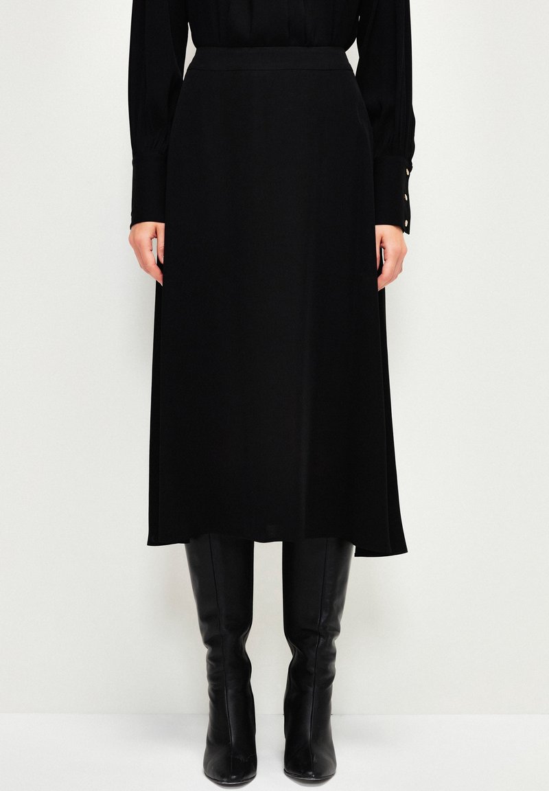 Jupe midi noire en tissu lisse, dotée d'une taille ajustée et d'une silhouette fluide, associée à des bottes noires montant jusqu'aux genoux.