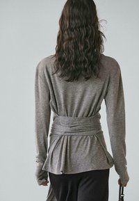 Szary top z długim rękawem, z taliowaniem i plisowanym tyłem. Miękki, teksturowany materiał o luźnym kroju, dopasowany przy dolnym brzegu.