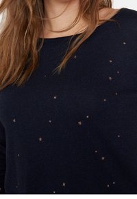Maglione a maglia blu scuro con scollatura ampia e stelle metalliche dorate disperse su tutta la superficie per un tocco di dettaglio in più.