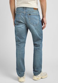 Light blue denim jeans with a straight leg cut, featuring two back pockets and a leather patch on the waistband. Textured fabric.