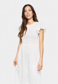 White dress with short ruffled sleeves, smocked bodice, and a flowing skirt featuring leaf-patterned eyelet details.
