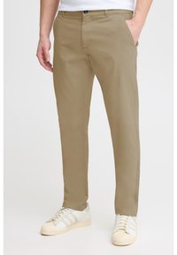 Khaki-Chinos mit geradem Schnitt, Fronttaschen und einem Bund mit Knopfverschluss, kombiniert mit weißen Sneakers.
