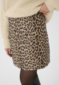 Falda de estampado de leopardo en tejido suave, con tonos de beige y marrón, y un diseño ligeramente acampanado. Combinada con un acogedor suéter en crema.