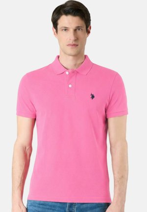 Uomo che indossa una polo a maniche corte di un rosa acceso con due bottoni e un logo scuro ricamato sul petto sinistro.