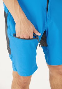 Blå shorts med en sidoficka med dragkedja, tillverkade av snabbtorkande material, med svarta tygdetaljer längs sidorna.