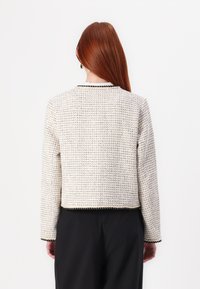 White textured jacket with a woven pattern, black trim at the neckline and hem, featuring long sleeves and a cropped design.