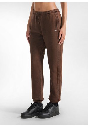 Pantaloni di felpa marroni con vestibilità affusolata, vita elastica, tasche laterali e polsini a coste, abbinati a sneakers nere.