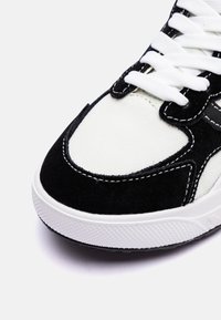 Sneaker in bianco e nero con tomaia in suede e tela, lacci bianchi piatti, cuciture a contrasto e suola in gomma testurizzata.
