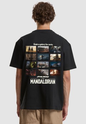 Osoba nosząca czarną koszulkę z siatką scen z The Mandalorian oraz tekstem "z dalekiej galaktyki" i "Star Wars The Mandalorian."