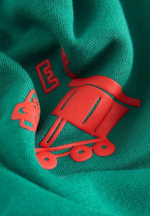 Tissu vert avec une texture douce, présentant une impression rouge bien visible d'un tramway de style cartoon et des lettres en gras.