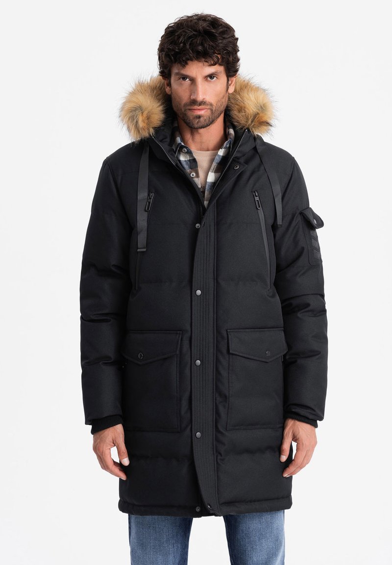 Parka nera imbottita con cappuccio foderato in pelliccia, dotata di tasche frontali con bottone, spalline e chiusura con zip. Tessuto testurizzato.