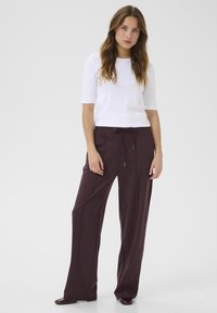 Camicia bianca aderente e pantaloni larghi marrone scuro con vita regolabile. Texture liscia e linee pulite, completati da scarpe lucide.