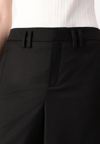 Pantalons noirs ajustés avec une texture lisse, deux poches avant et une taille plate avec deux passants de ceinture.
