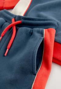 Bomuldsjoggers med en marineblå bund og røde samt hvide detaljer, snøre i taljen og sidelommer. Blød tekstur og afslappet design.