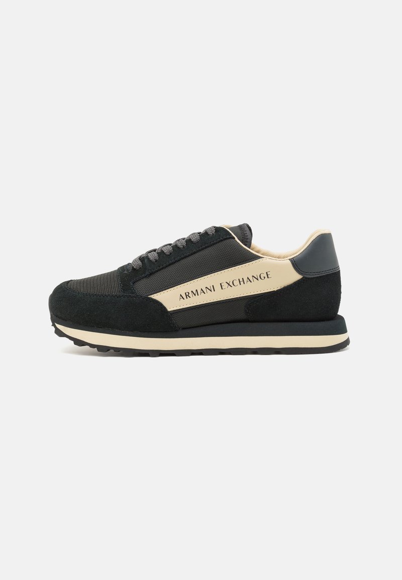Adidași negri din material de suede și plasă, cu accente bej, talpă plată din cauciuc și un logo pe lateral. Sireturi de culoare gri închis. Design clasic.