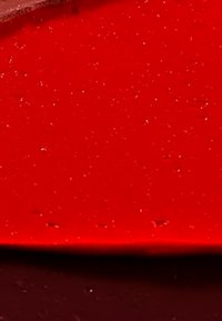 Superficie rossa lucida con una texture liscia, caratterizzata da dettagli di fine glitter distribuiti uniformemente e un bordo rosso scuro.