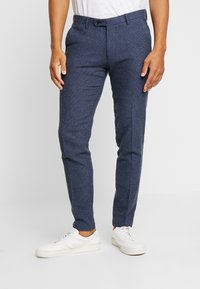 Tailored navy trousers in textured fabric, featuring a slim fit, belt loops, front pockets, and a button closure. Paired with white sneakers.