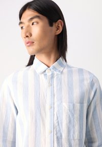 Chemise boutonnée à rayures bleu clair et blanche en lin, dotée d'une poche poitrine et d'un col classique, avec une coupe décontractée.