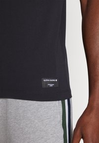 Μαύρο κοντομάνικο μπλουζάκι φτιαγμένο από ελαφρύ ύφασμα, με ριγέ ετικέτα που έχει το λογότυπο "BJÖRN BORG" στη μέση.