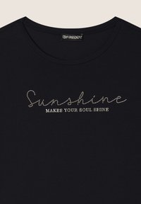 Camiseta de algodón negra con cuello redondo; presenta rhinestones plateados que forman la frase "La luz del sol HACE BRILLAR TU ALMA" en el pecho.