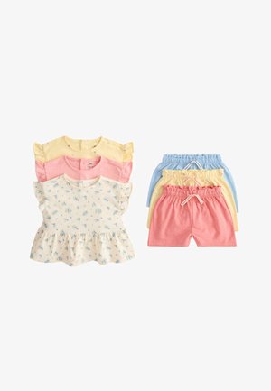 Tre set di completi per bambina piccoli con magliette e pantaloncini nei colori giallo pastello, rosa e blu, con stampe floreali sulla maglietta crema, disposti in piano.