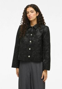 Veste noire à motifs floraux avec un col, fermeture à boutons sur le devant et manches longues ; comporte des boutons argentés et un tissu texturé.