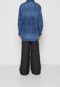 Modrá džínová košile s volnějším střihem, s zadním dílem, manžetami na knoflíky a kontrastními širokými černými kalhotami.