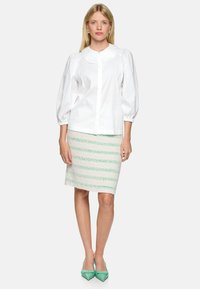White collared puff-sleeve blouse paired with a light green striped pencil skirt. The model wears green pointed-toe heels.