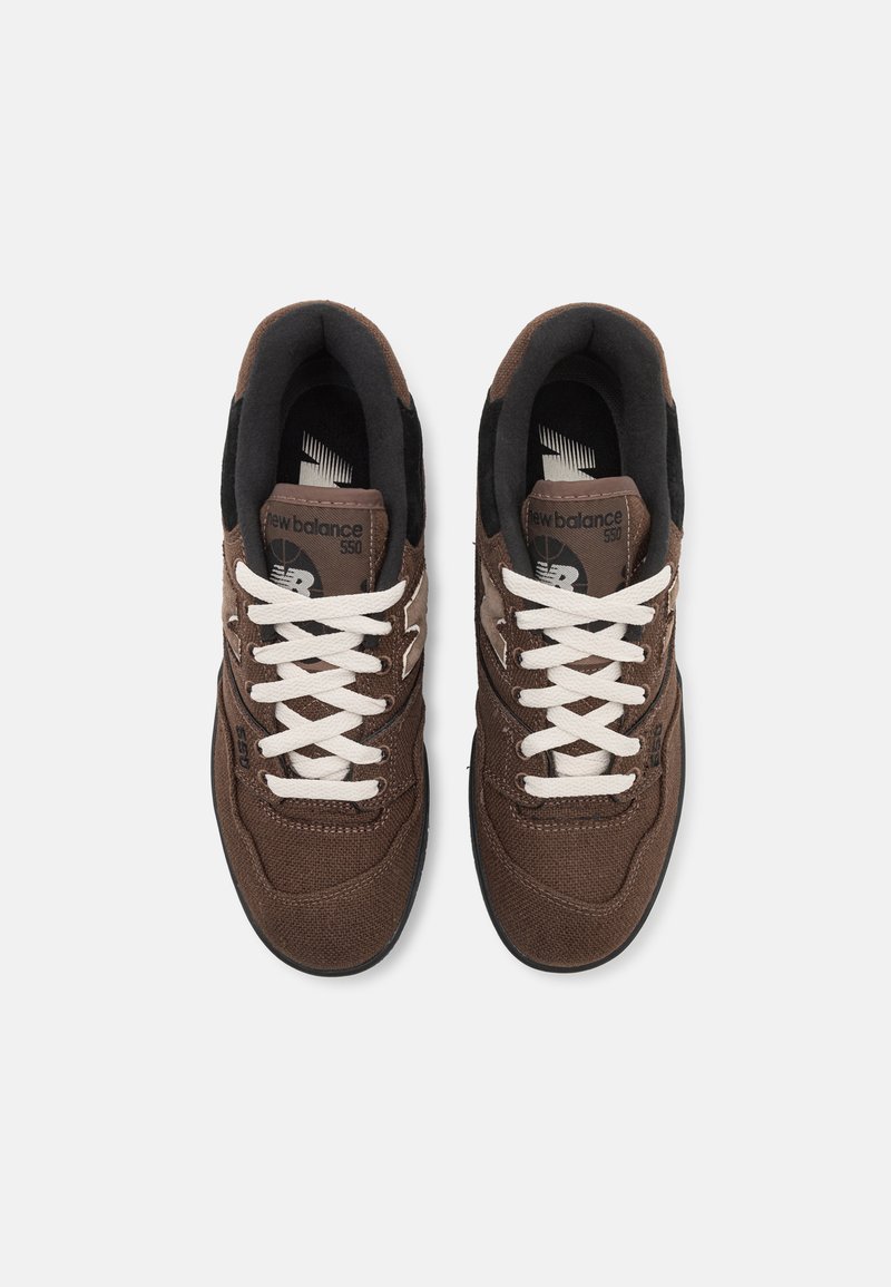 Zapatillas de lona marrones con cordones blancos, con punta redonda, superficie texturizada y detalles negros en el collar y la lengüeta, logo en el costado.