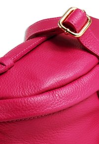 Heldere roze leren tas met een zachte, gestructureerde uitstraling, voorzien van een aansluitende bovenkant en een gouden gesp als accent op de riem.