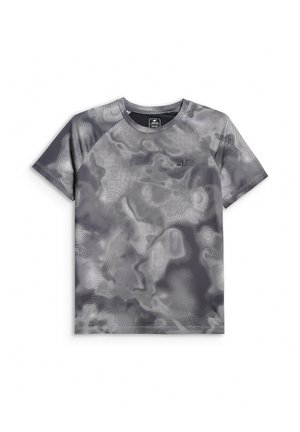 Dziecko ubrane w szary T-shirt z wzorem, czarne szorty, białe skarpety w czarne paski, czarno-białe trampki i beżową opaskę na głowę, stoi.
