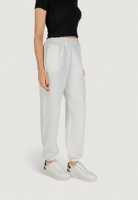 Pantalon de jogging blanc à taille élastique avec poches latérales, bas resserrés et texture lisse, associé à des baskets blanches avec des accents noirs.