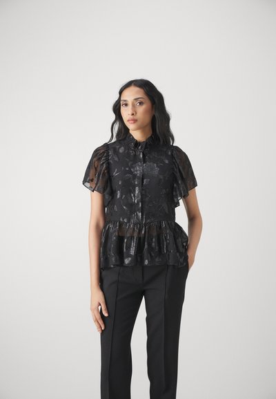 Schwarze Peplum-Bluse mit kurzen, durchsichtigen Ärmeln, strukturiertem Blumenmuster und knöpfbarem Ausschnitt; kombiniert mit schwarzen Hosen.