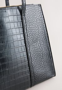 Czarna torebka z fakturą wzoru krokodyla, błyszczącym wykończeniem, usztywnionym kształtem oraz solidnymi, płaskimi uchwytami i złotym zamkiem błyskawicznym.