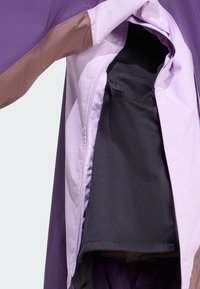 Lila Jacke mit braunen Akzenten. Das Innenfutter ist mit einem schwarzen Netzfutter und einer Reißverschlusstasche ausgestattet. Glattes Material mit leichtem Design.
