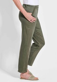 Olivgrüne, gerade geschnittene Hose mit Fronttaschen und Gürtelschlaufen, aus weichem Stoff. Getragen mit hellen Sandalen.