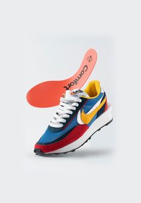 Baskets bleues et rouges avec des accents jaunes et blancs. Comprend une tige texturée, un col rembourré, et une semelle intérieure amovible orange étiquetée "Confort."