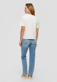 Camiseta blanca de manga corta con rayas verticales en gris claro, combinada con unos vaqueros azules de corte holgado y zapatillas de piel clara.