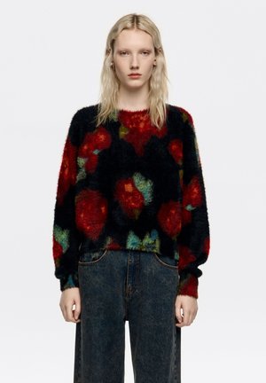 Puszysty czarny sweter z wyrazistym czerwono-zielonym kwiatowym wzorem. Okrągły dekolt i długie rękawy, zestawiony z ciemnymi, wysokim stanem jeansami.