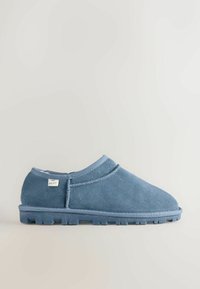 Weicher Slip-On-Schuh aus blauem Wildleder mit flexiblem Gummisohlen und niedrigem Knöchelschnitt, der an der Seite ein kleines weißes Stoffetikett aufweist.