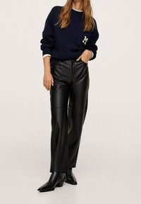 Suéter de punto azul marino con logo "M", combinado con pantalones de imitación cuero negros de cintura alta y botines negros de punta afilada. Textura suave.