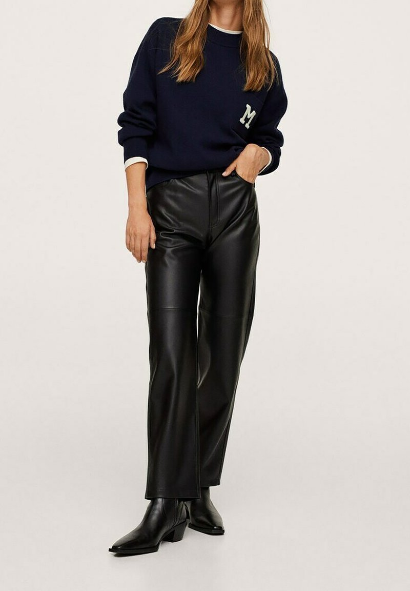 Suéter de punto azul marino con logo "M", combinado con pantalones de imitación cuero negros de cintura alta y botines negros de punta afilada. Textura suave.